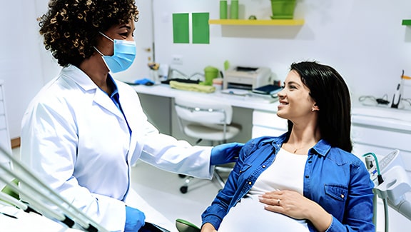 A young pregnant woman in a denim long sleeved shirt getting a consultation from a female dentist
