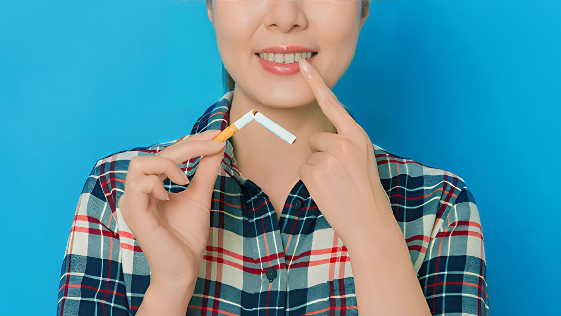 A woman point to her teeth as she holds a broken cigarette in her other hand.
