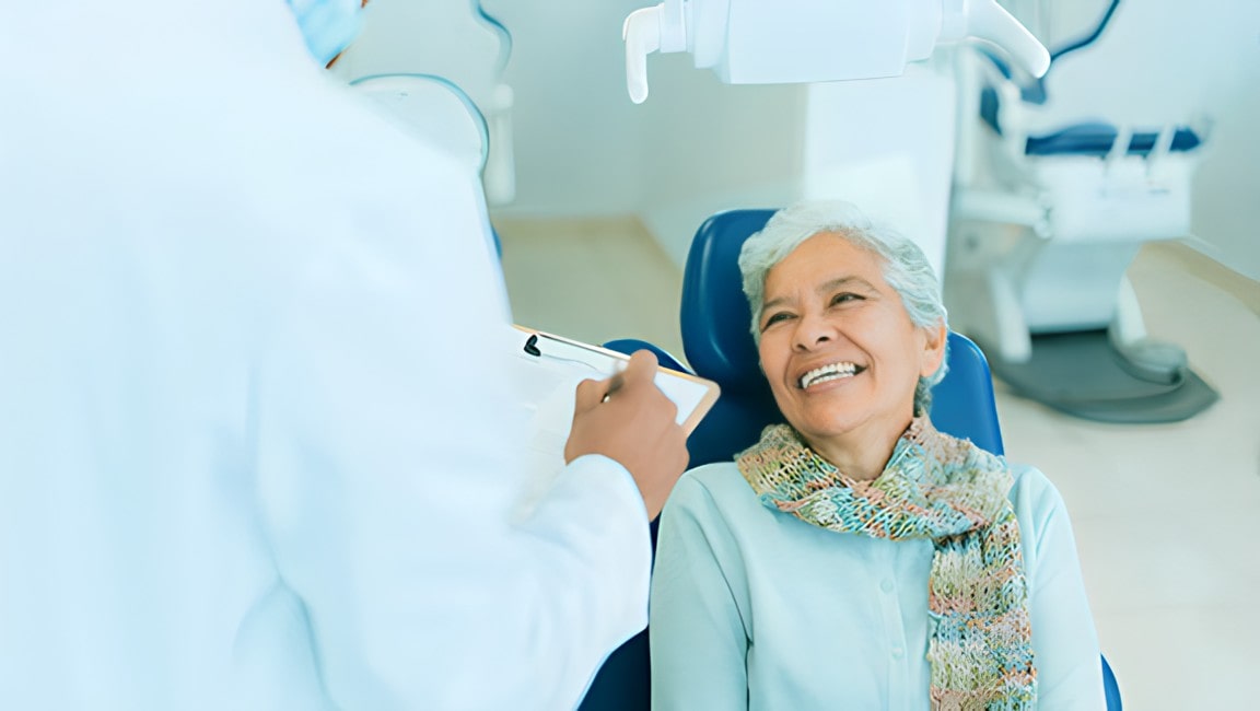 A happy senior female patient sitting on a dental examination chair, looking at the male dentist and smiling.