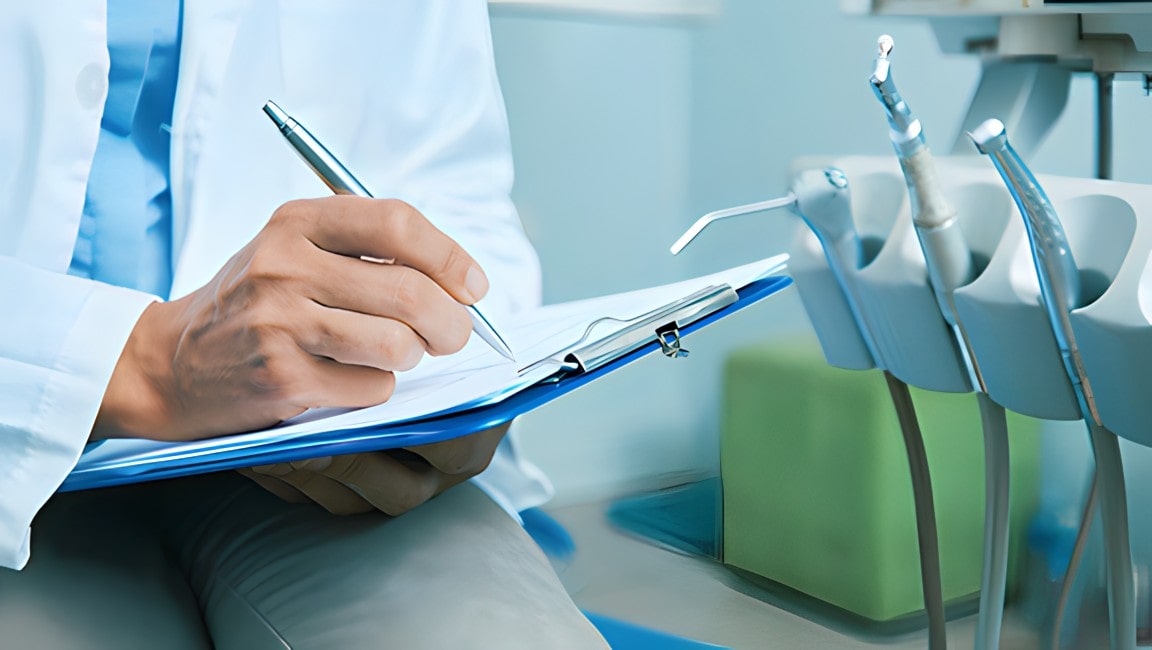 A dentist writing notes and creating a pretreatment estimate on a clipboard.