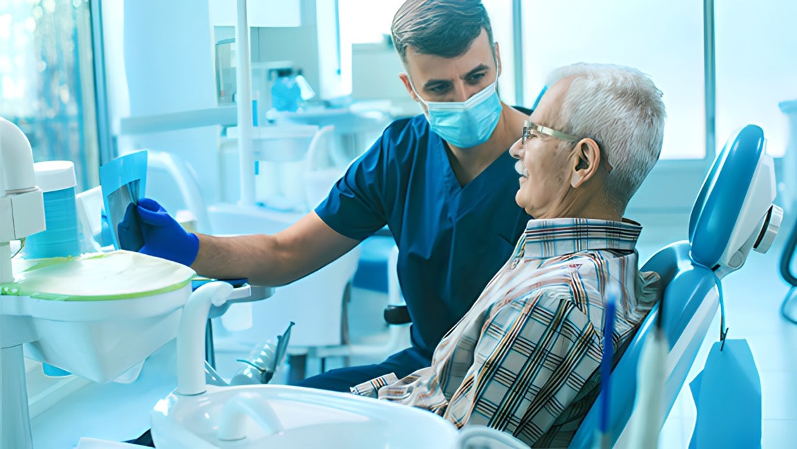 Senior man sitting in a dental chair, while his dentist reads him out an x-ray scan